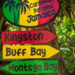 Colorful directional signs to Jamaican destinations in a tropical setting.