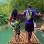 Couple walking on bamboo raft, tropical setting.